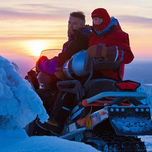 Un couple en motoneige s’arrête un instant, le regard tourné vers l’objectif, complices dans la blancheur hivernale