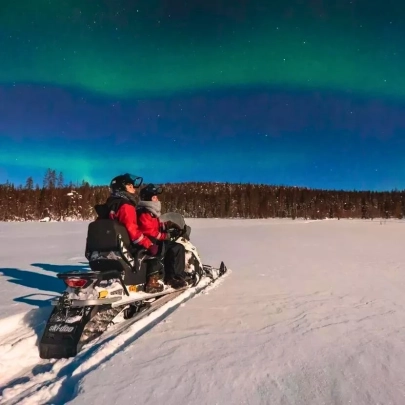 Motoneige roulant dans la nuit arctique sous un ciel étoilé teinté d’aurores boréales à Muonio