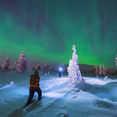 Promeneurs en raquettes traversant la neige, sous un ciel nocturne illuminé par les aurores boréales à Muonio