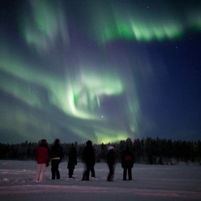 Petit groupe réuni autour d’un feu crépitant sous les aurores boréales, dans un paysage enneigé et paisible à Muonio
