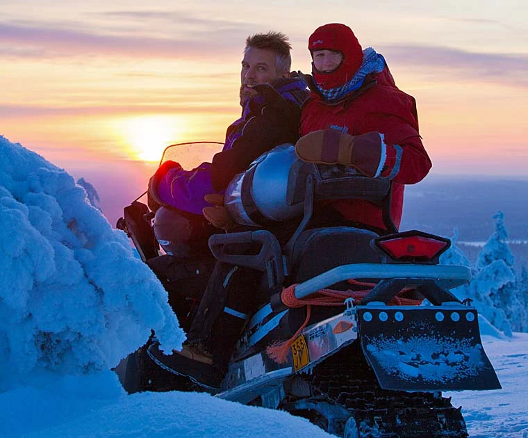 Un couple en motoneige s’arrête un instant, le regard tourné vers l’objectif, complices dans la blancheur hivernale