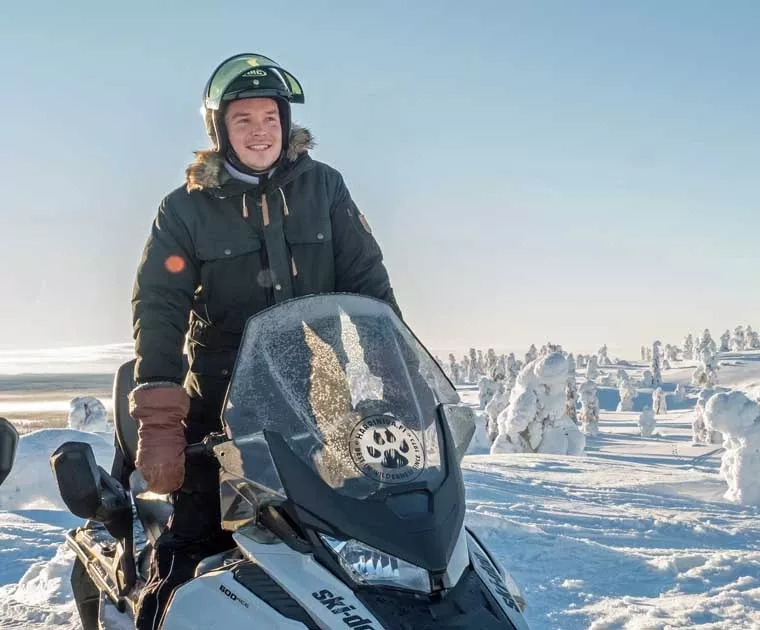 Homme souriant debout sur une motoneige en Laponie